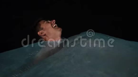 可爱的年轻人躺在蓝色玻璃纸下模仿水大声笑出来视频的预览图
