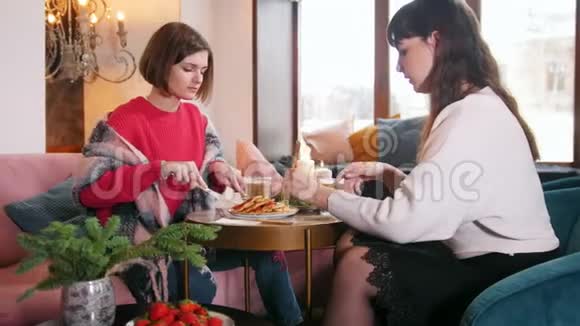 两个年轻的女人坐在咖啡馆里边吃煎饼边说话视频的预览图