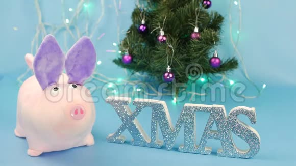 一个人在蓝色背景上放了一只粉红色的小猪背景上放了一棵圣诞树个玻璃杯视频的预览图