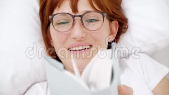 红发女孩在白床上看书顶部视图视频的预览图