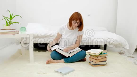 漂亮的年轻女人坐在客厅的地板上用大量的书即兴创作视频的预览图