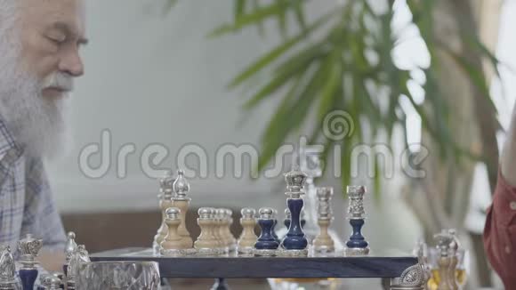 两个成熟的老朋友坐在家里下棋高加索老人邻居在室内愉快地下棋视频的预览图