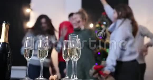 新年庆典人们在圣诞树前跳舞时会从餐桌上拿香槟笛子视频的预览图