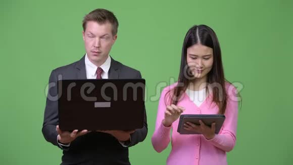 年轻的亚洲妇女和年轻的商人一起使用笔记本电脑和数码平板电脑视频的预览图