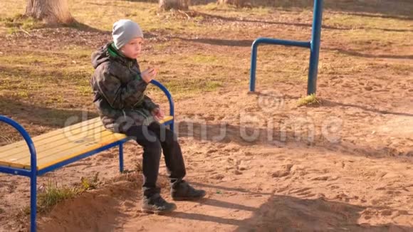 男孩坐在公园的长凳上吃华夫饼侧视视频的预览图