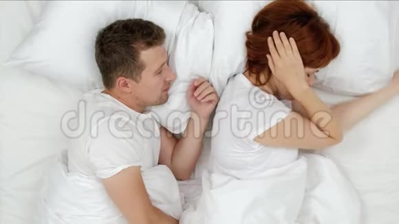 在喧闹的夜晚打鼾的男人哽咽着大声叫醒他的妻子她用枕头闭上耳朵上文视视频的预览图