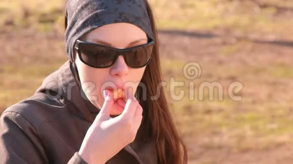 年轻的黑发女人戴着太阳镜在公园的长凳上吃橘子特写的脸视频的预览图