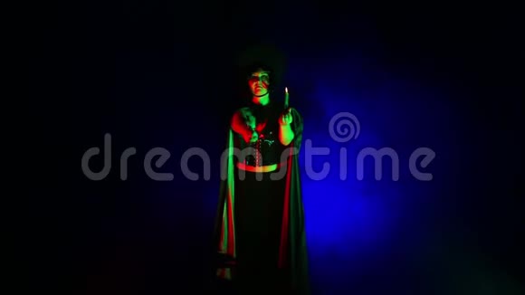 一个年轻的女巫在灯光下在烟雾云中黑色手里拿着蜡烛从事魔法视频的预览图