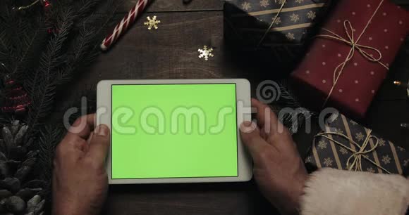 圣诞老人手里拿着绿色屏幕的白色平板电脑另一只手把一些礼物盒放在视频的预览图