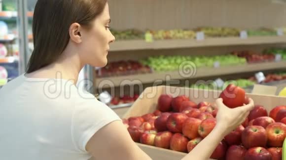 年轻女子在杂货店买健康食品素食女孩选择新鲜的红苹果视频的预览图