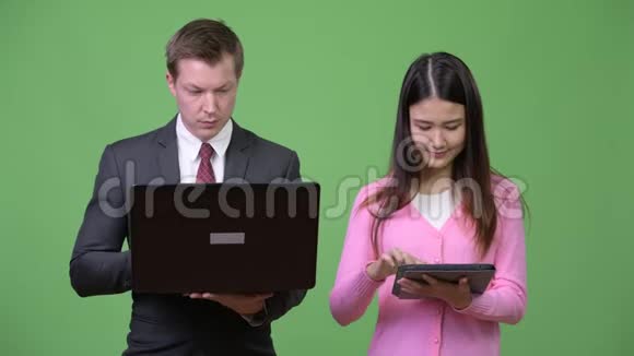 年轻的亚洲妇女和年轻的商人一起使用笔记本电脑和数码平板电脑视频的预览图