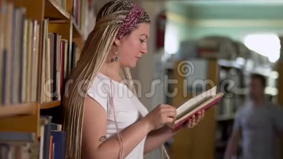 美丽的女孩正在图书馆翻阅一本书视频的预览图