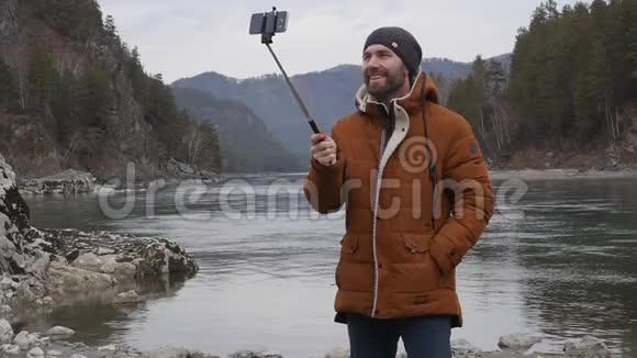 大胡子的游客正在一条山河的河岸上用手机播放视频慢动作视频的预览图
