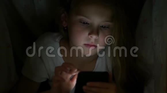 一个孩子躲在毯子下面用智能手机上网视频的预览图