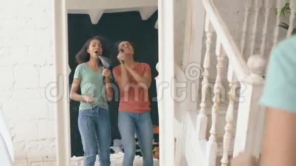 混合种族年轻有趣的女孩跳舞用吹风机和梳子在镜子前唱歌姐妹们玩得开心视频的预览图