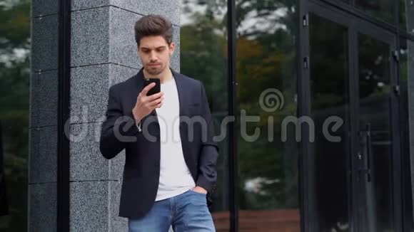 美国帅哥在办公大楼背景下智能手机上使用商务应用程序穿西装的年轻商人视频的预览图