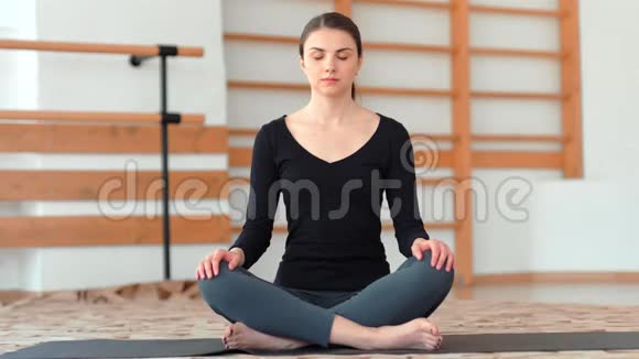 有吸引力的年轻女性在练习室休息时坐在瑜伽莲花的位置视频的预览图