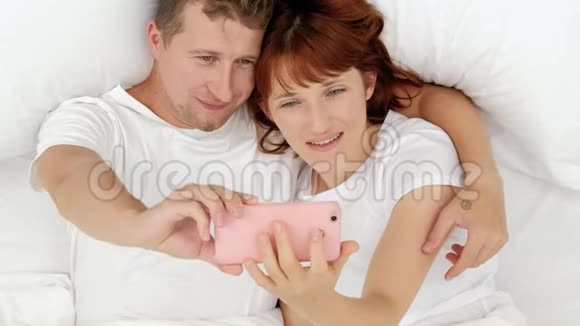 这对年轻有魅力的夫妇躺在床上在智能手机上自拍视频的预览图