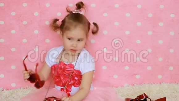 心形太阳镜一个小女孩打扮成红色的包和鞋子有趣的孩子粉红色背景视频的预览图