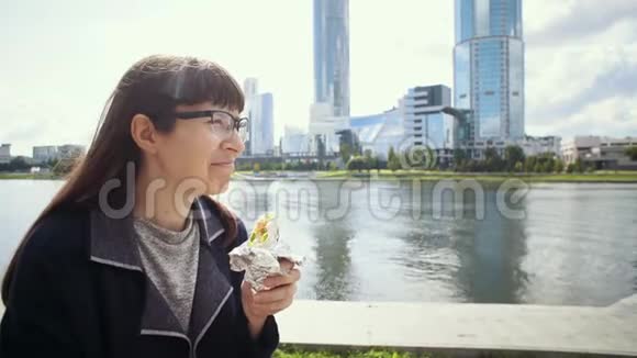 快乐的女商人在市中心河岸附近吃多纳串视频的预览图