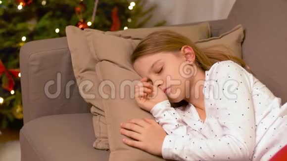 小女孩睡在圣诞树旁的沙发上视频的预览图