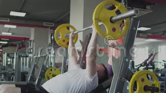 在健身房为男子提供女子教练的个人训练厚肥胖的家伙和私人教练做身体抽搐和视频的预览图