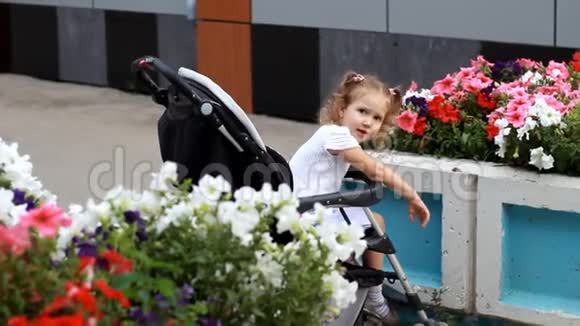 小女孩坐在婴儿车里和妈妈一起散步公园里开着漂亮的花视频的预览图