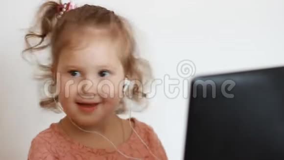 一个戴着耳机的小可爱女孩微笑着看着屏幕监视器电脑看电视看视频看卡通或者视频的预览图