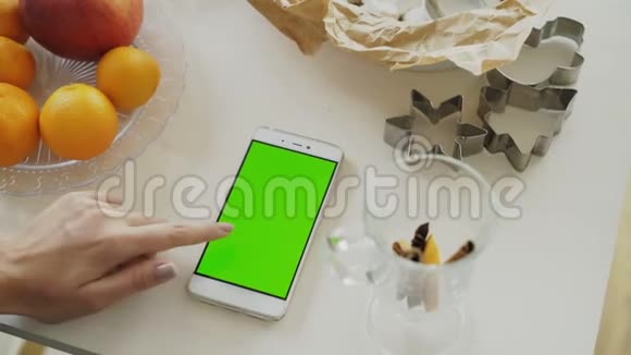 家厨房餐桌上有绿色屏幕的女士手游智能手机特写视频的预览图