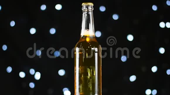 淡啤酒放在清澈的瓶子里在黑色背景上旋转明亮的灯光下视频的预览图