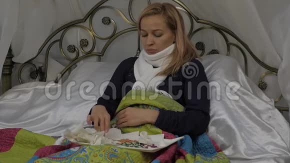 一个生病的女人躺在床上脖子上围着一条温暖的围巾在感冒或感冒时吹鼻涕视频的预览图