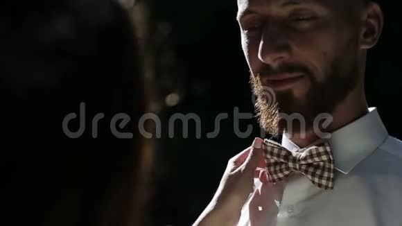 微笑的新娘把蝴蝶结固定在新郎衬衫上慢动作的快乐时刻视频的预览图