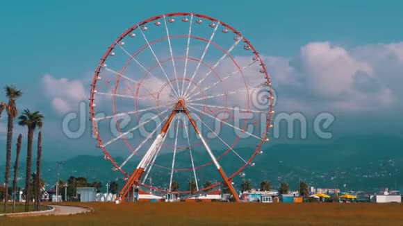 摩天轮在度假小镇棕榈树附近的云层映衬着蓝天阳光明媚视频的预览图