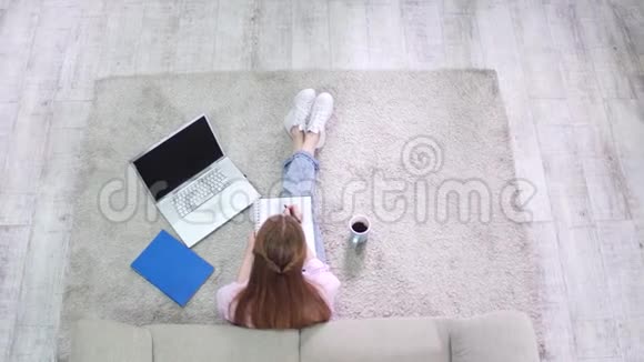 从上面看学生女孩坐在地毯上写在笔记本上视频的预览图