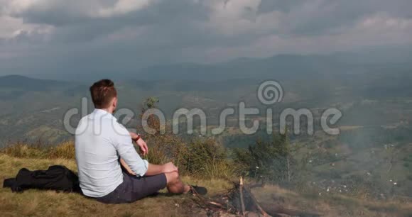 篝火燃烧着一个孤独的人坐在山顶上看彩虹视频的预览图