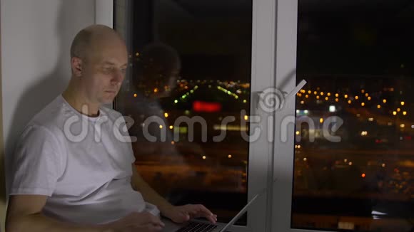 晚上在窗台上使用笔记本电脑的自信男士遥控器视频的预览图