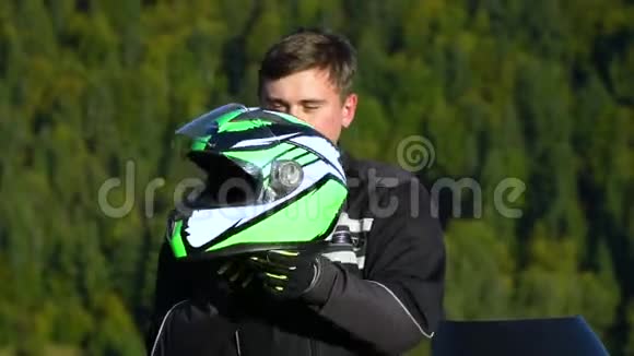 一个骑摩托车的人带着摩托车在山上的年轻帅哥特写镜头他戴着头盔视频的预览图