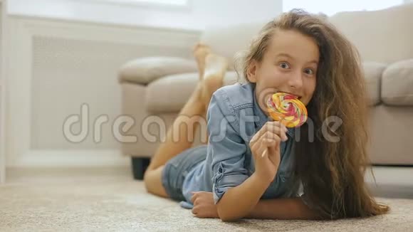 美丽的金发少女和糖果一个活泼可爱的女孩在窗户前的沙发附近有一个大甜棒棒糖视频的预览图