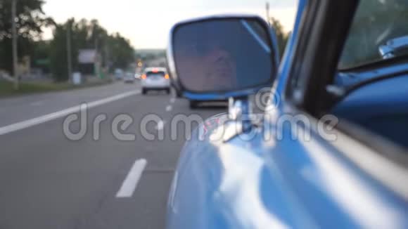 严重男司机反映在移动复古车的左侧镜子中开着蓝色老式汽车的年轻人视频的预览图