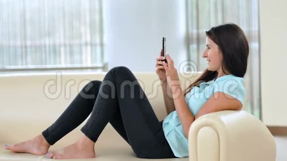 年轻的商务女性坐在沙发上使用智能手机女孩网上购物博客查看电子邮件聊天视频的预览图
