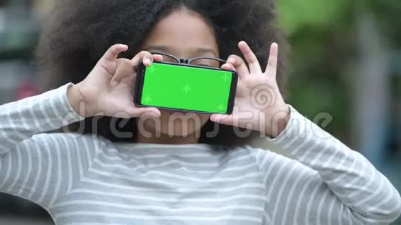年轻可爱的非洲女孩带着非洲头发在户外的街道上展示电话视频的预览图