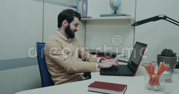 费斯的工作人员坐在他的桌子上敲击他的笔记本电脑的键盘有一个专注和微笑的脸视频的预览图