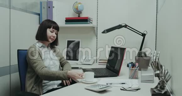 小办公室角落里的特写镜头年轻女子在办公桌前休息喝着咖啡微笑着开始工作视频的预览图