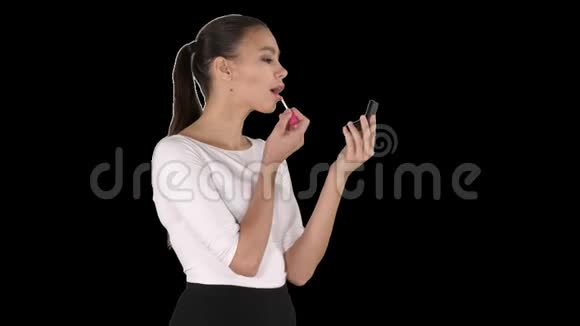 美丽的女人把嘴唇涂上粉红色看着镜子里的阿尔法通道视频的预览图