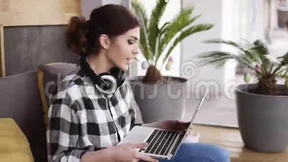 一个时髦的黑发女孩手里拿着一台笔记本电脑在沙发上扑通一声开始打字戴在脖子上现代视频的预览图