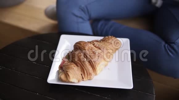 一个穿着休闲服的漂亮黑发女人从盘子里拿出一个大羊角面包三明治咬掉一块你的眼睛视频的预览图