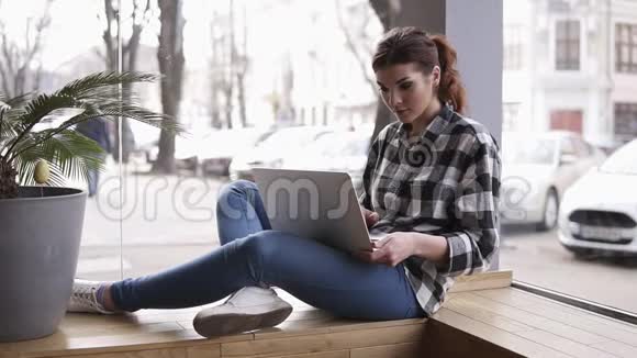美丽的年轻黑发女人在她的笔记本电脑上工作坐在靠近窗户的一家现代化内部的咖啡馆里模糊的视频的预览图