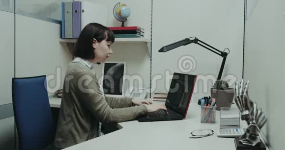办公室里的年轻女性坐在办公桌前在笔记本上敲击键盘红色史诗视频的预览图