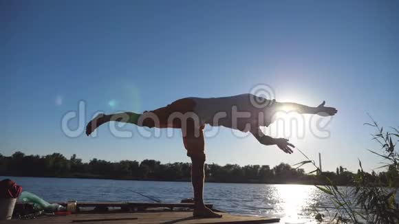 站在瑜伽馆前的年轻人的剪影摆在湖边的木制码头上在大自然训练运动的家伙运动员在做视频的预览图