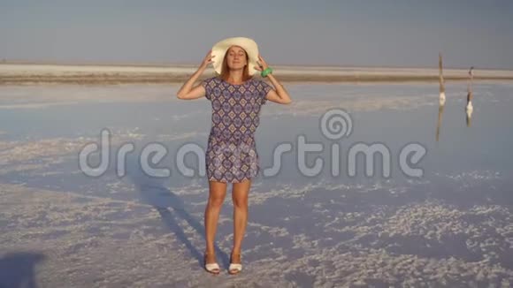 戴着白帽子欣赏日落的苗条女孩盐湖的木制盐柱视频的预览图
